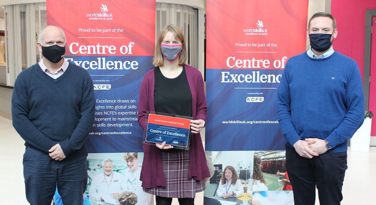 Three people wearing masks in front of WorldSkillsUk Centre of Excellence Banners